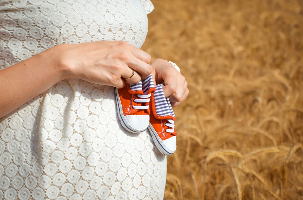 Pregnant woman holding tiny baby shoes — pregnancy due date calculator article