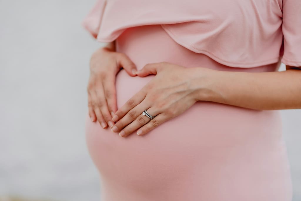 Expecting mother in a soft pink dress with hands resting on her bump — first trimester week by week