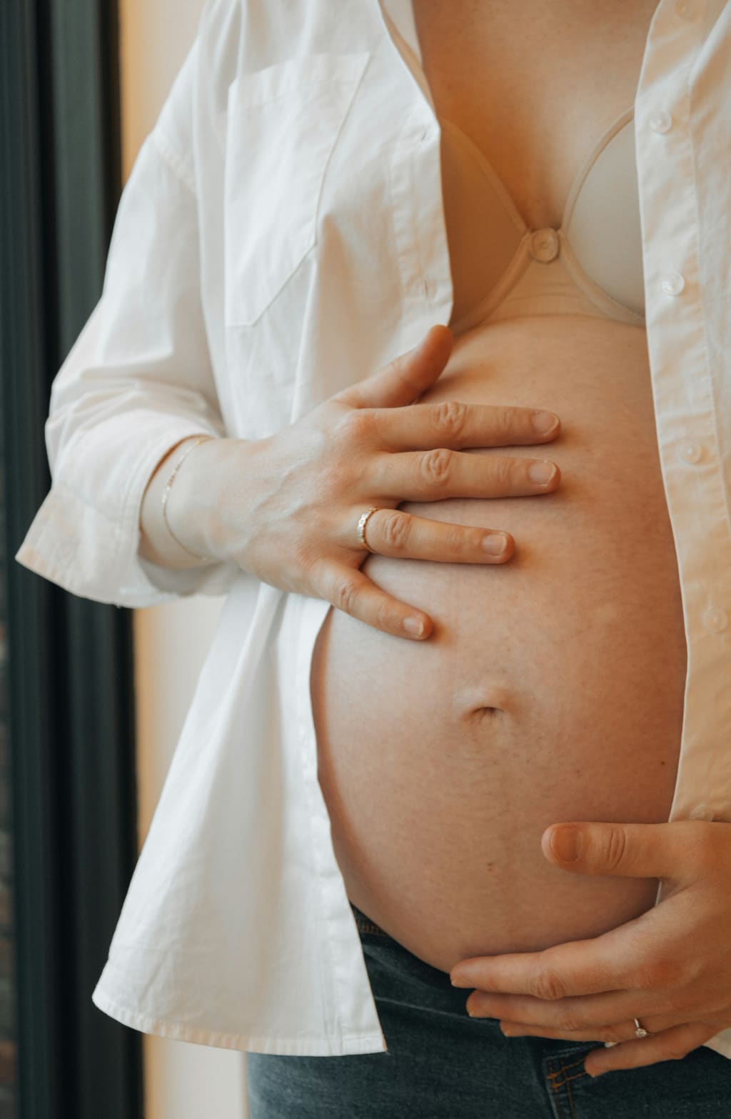 Late pregnancy bump with hands resting on it in soft daylight — mucus plug and approaching labour