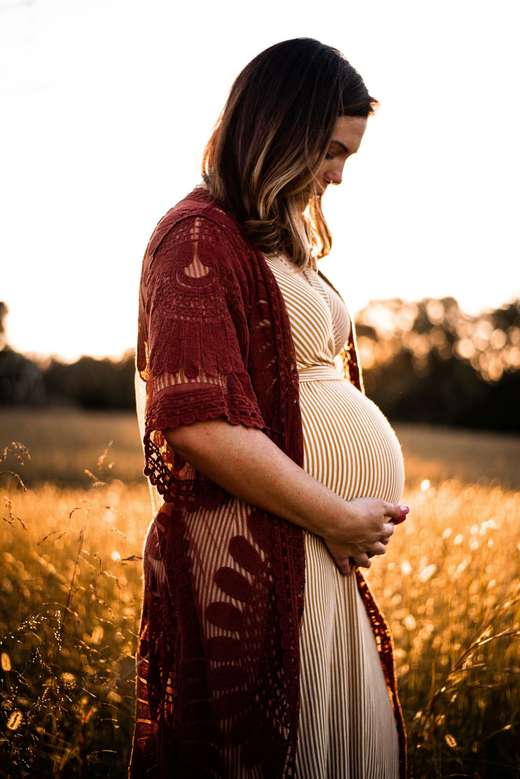 Woman in late pregnancy holding her bump in a sunlit field — signs labour is near
